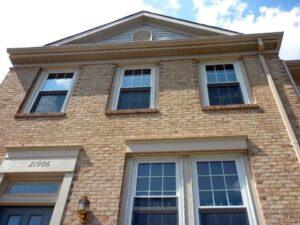 A close-up view of the front of a two-story brick townhouse with three upper windows, two lower windows, a door marked 21906, an exterior light fixture, and a cloudy sky above.