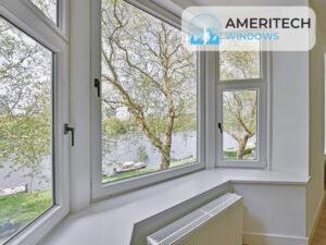 A bay window with large triple pane windows overlooking a river and trees, featuring a white windowsill and radiator below. The Ameritech Windows logo appears in the top right corner.